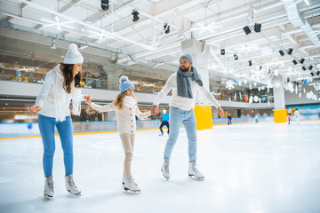 happy family holding hands while skating together on ice rink - obrazy, fototapety, plakaty