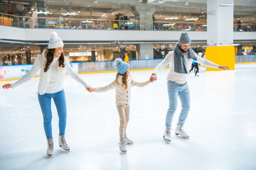 family in sweaters holding hands while skating together on ice rink