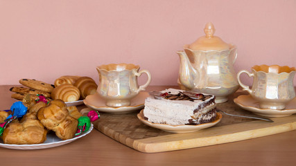 Breakfast. Two cups of tea, teapot, a piece of cake on a saucer, candy, cookies.