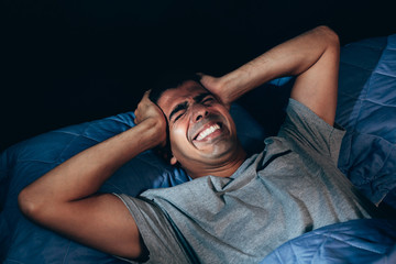 Handsome young man suffering from headache while lying in bed at night