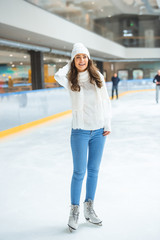 smiling young attractive woman in knitted sweater skating on ice rink alone