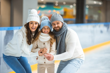 portrait of smiling parents and daughter in sweaters looking at camera on skating rink