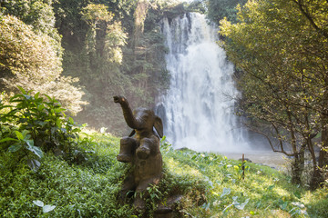 Naklejka na ściany i meble Statue of happy baby elephant with waterfall on the background