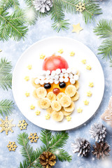 Fototapeta na wymiar Santa Claus face made of fruits and marshmallow on a plate. Christmas food for children. Top view