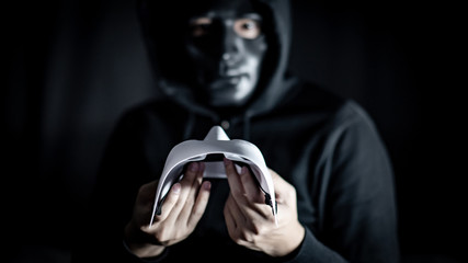Mystery hoody man wearing broken black mask holding white mask. Anonymous social masking. Major...