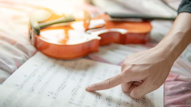 Musician hand pointing on sheet of music note and vintage violin on flowery pink bed in the bedroom. Playing music instrument at home concept