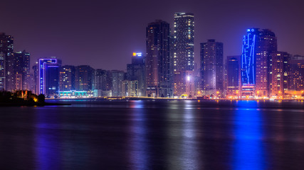 Fototapeta na wymiar Beautiful view to Sharjah city center lights skyline at night, United Arab Emirates. Skyscrapers are reflecting in water
