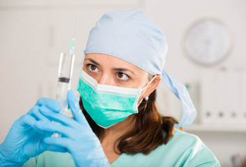 Female nurse in mask holding syringe for injection in hospital