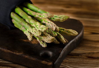 Green juicy asparagus is lying on a wooden board on a brown wooden table.