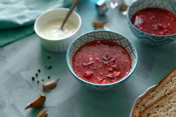 Red borscht soup in blue bowl with sour cream, bread, garlic and spices on blue wooden background. Top view. Flat lay