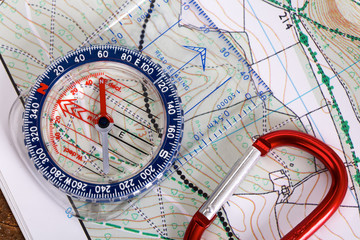 Close up of a modern plastic compass with scales and rulers, wooden background and detailed hiking map