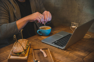 man hands working on laptop in cafe eating sandwich drinking coffee