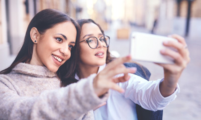 Obraz premium two beautiful cheerful women making selfie by the phone in the central part of city
