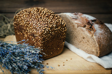 Baked homemade rye dark bread with coriander seeds and lavender on rustic wooden table background.