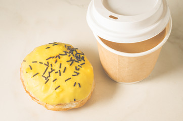 donut in yllow glaze and a paper coffee cup/donut in yellow glaze and a paper coffee cup on a white table. Top view
