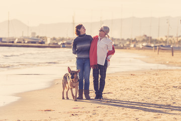 Beautiful older mom and mature daughter walking their german shepard dog on beach at autumn sunset
