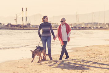 Beautiful older mom and mature daughter walking their german shepard dog on beach at autumn sunset