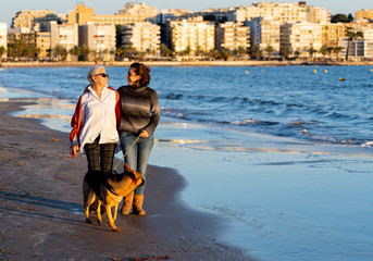 Beautiful older mom and mature daughter walking their german shepard dog on beach at autumn sunset