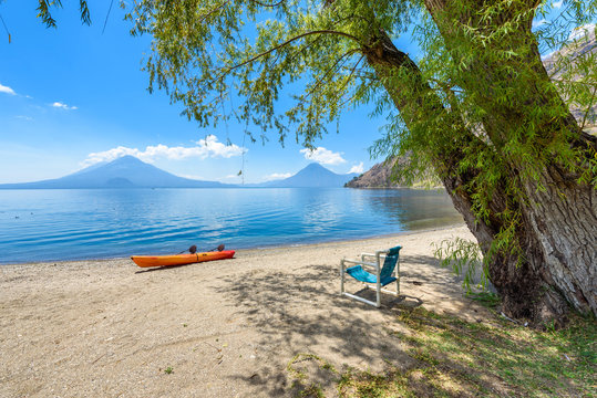 Paradise beach with chair and kayak at lake Atitlan, Panajachel - Relaxing and recreation at beach with vulcano landscape scenery in the highlands of Guatemala