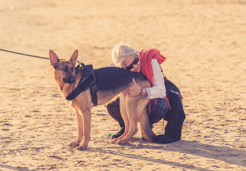 Happy attractive senior woman with her german shepard dog playing on the beach at autumn sunset