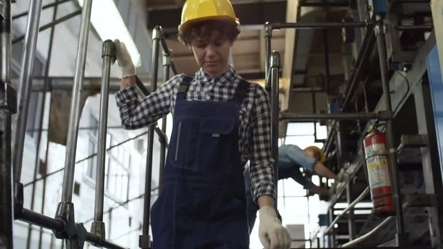 Young female industrial worker in overall and hardhat walking through printing plant and looking around