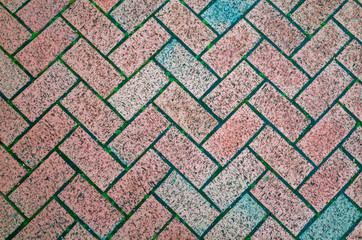 A close-up of block paving bricks set in a herringbone pattern with faded colours.