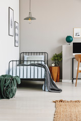 Metal basket with grey blanket next to single bed with blue bedding in stylish bedroom interior,...