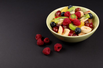 Fruit Salad in Green Bowl and raspberries on black Table, side View. copy space.