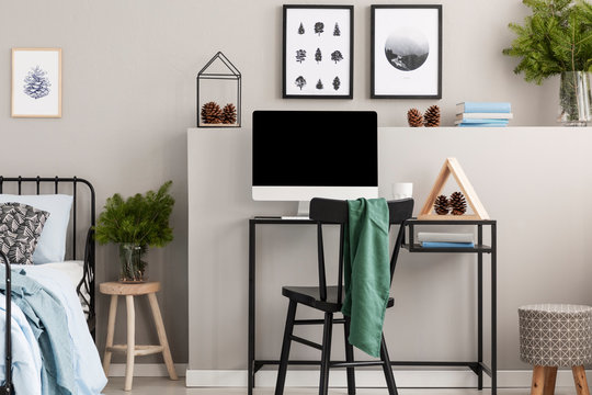 Grey blanket on black wooden chair at industrial desk with computer in scandinavian grey teenager's bedroom