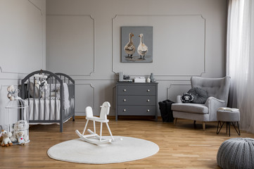 White rocking horse on rug in grey baby's bedroom interior with poster above cabinet. Real photo