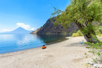 Paradise beach with chair and kayak at lake Atitlan, Panajachel - Relaxing and recreation at beach with vulcano landscape scenery in the highlands of Guatemala