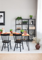 Black chairs at wooden table in grey dining room interior with flowers and brown carpet. Real photo