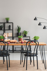 Black chairs at wooden table with food in grey dining room interior with lamp and plants. Real photo