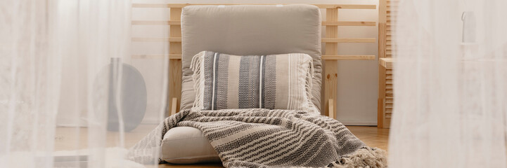 Futon armchair with pillow and blanket in real photo of bright living room interior with white...