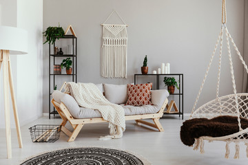 Handmade macrame on the empty wall of bright beige living room with comfortable couch with pillows...