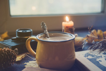 Yellow mug with autumn leaves, a book and candles. The concept of comfort and warmth.
