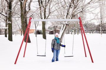 woman swinging and having fun on a swing in a snowy park on a cold winter day
