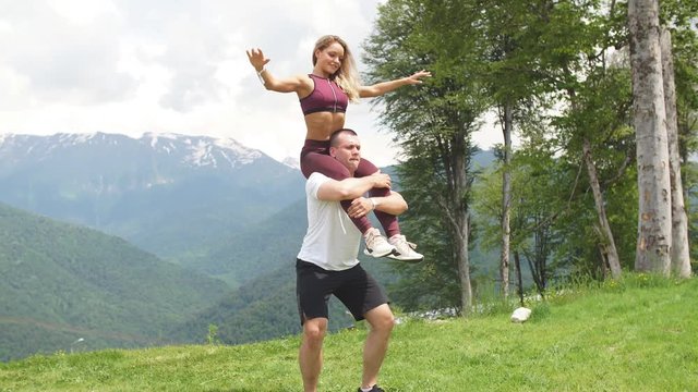 Athletic woman doing exercise with her male partner outdoors over high mountains in background