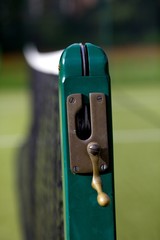 Tennis court net with green post with handle to move net higher or lower.
