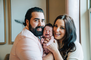 Smiling parents holding crying newborn baby