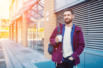 Handsome young man in purple winter jacket drinking coffee. The guy drinking coffee on the street. Sun flare