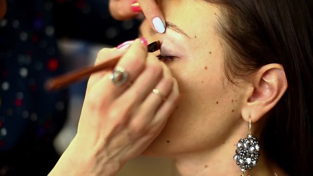 Make-up artist working in studio with young beautiful woman.