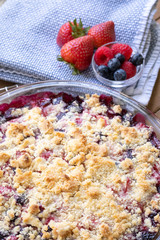Buckled crust of berry cobbler on a wood table, with spring berries in the background