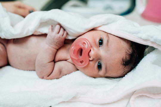 Newborn wrapped in a towel with a pacifier in her mouth