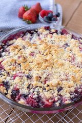 Close up on a berry cobbler on a wire cooling rack, with spring berries in the backround