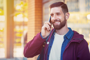 Young man wearing winter clothes with a smartphone in his hand, walking in the street. Sun flare