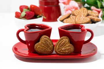 two red coffee cups and heart shaped cookies on white table
