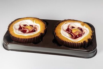 Sweet muffin with fruit jelly and cream. Packaged in a plastic container. Ready for sale. Closeup on white background.