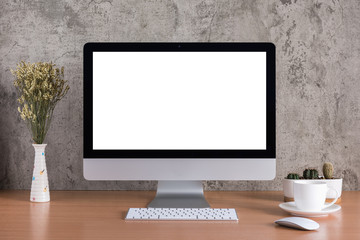 Blank screen of all in one computer with dry flowers, coffee cup and cactus vase on raw concrete background