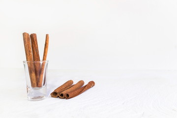 Cinnamon in glass and cinnamon sticks on white wooden table and white background, image with copy space.